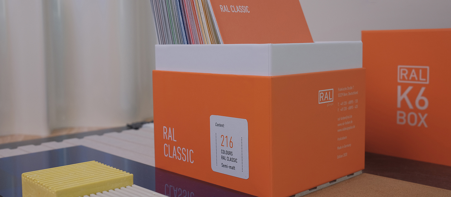 RAL K6 Box. Die Box ist geöffnet, mittig auf dem Bild und schräg positioniert. Im Vordergrund sind einige Gestaltungs-Accessoires zu erkennen. Im Hintergrund befindet sich der Deckel der Box so aufgestellt, dass die Aufschrift "RAL K6 Box" lesbar ist. | RAL FARBEN

RAL K6 Box. The box is open, positioned in the middle of the picture and at an angle. Some design accessories can be seen in the foreground. In the background, the lid of the box is positioned so that the inscription "RAL K6 Box" is legible. | RAL COLOURS